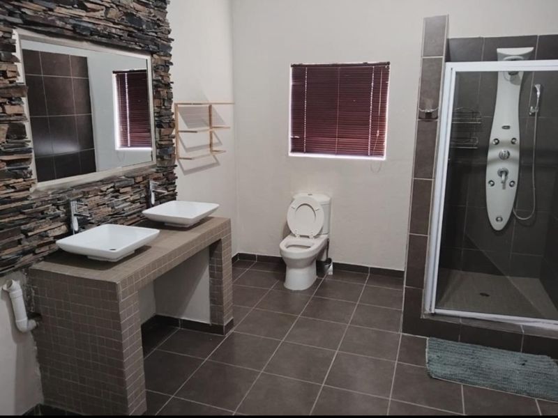 A spacious bathroom featuring a double vanity with vessel sinks, a stone feature wall, and a walk-in shower with a modern shower panel.