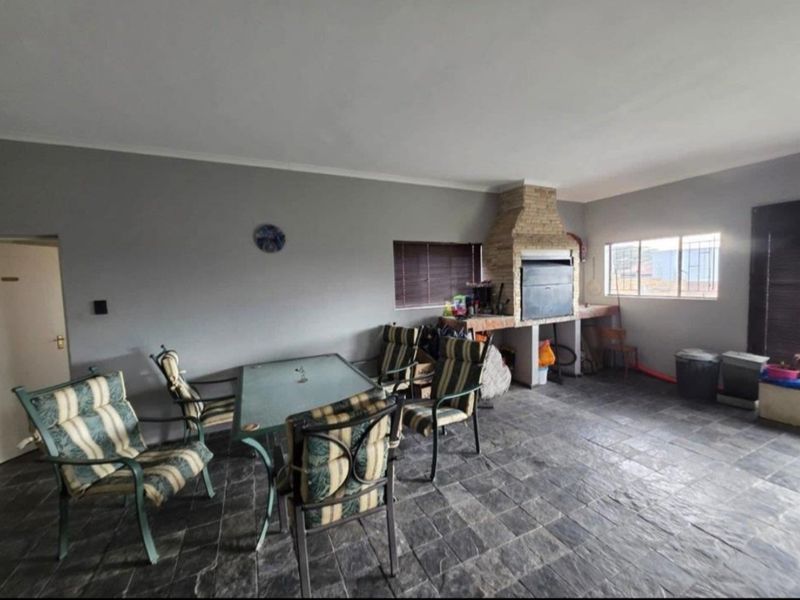 Covered patio area featuring stone tile flooring and a built-in brick braai, providing a functional space for outdoor entertaining.