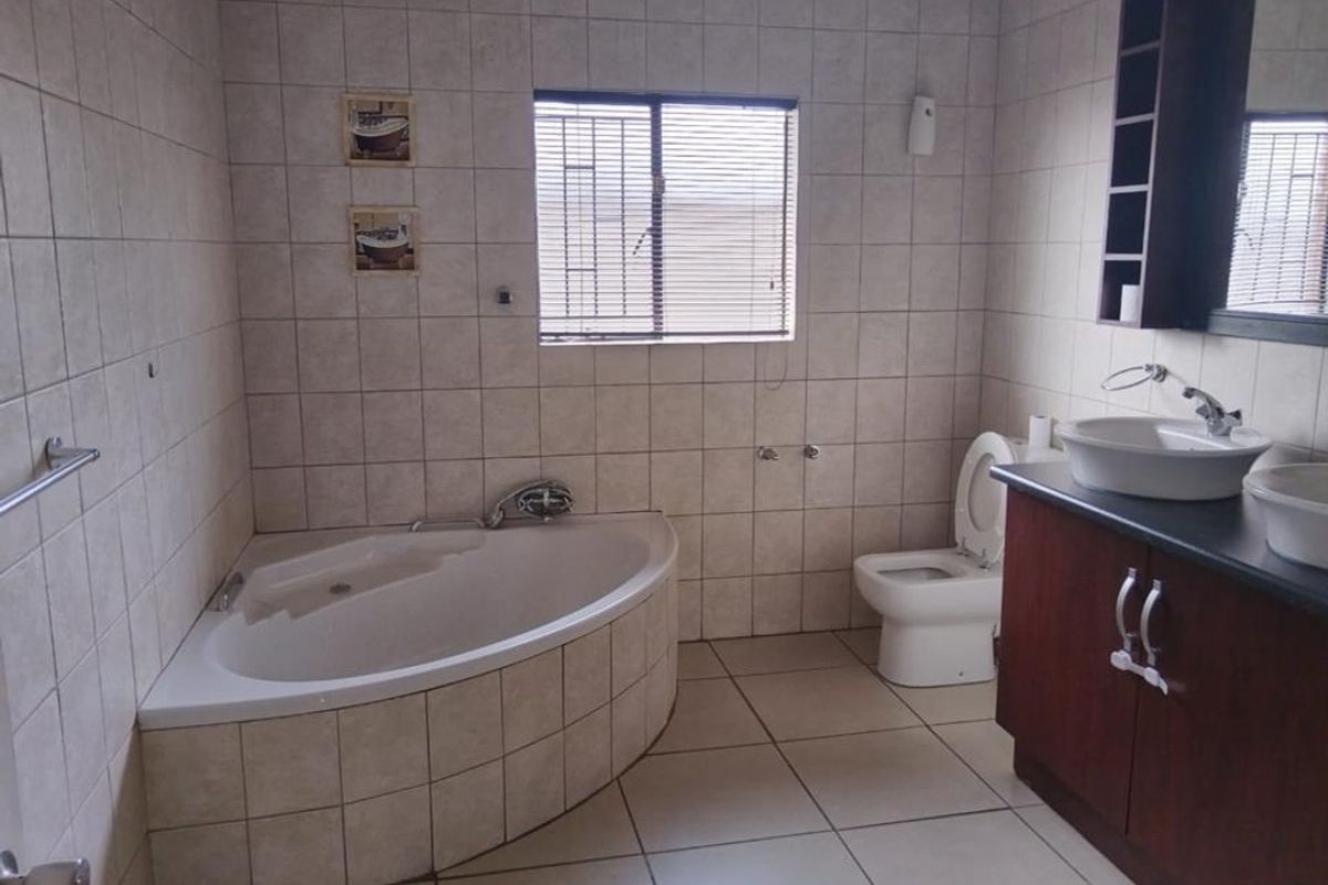 A functional bathroom featuring a corner bathtub, dual vessel sinks on a vanity cabinet, and tiled finishes throughout.