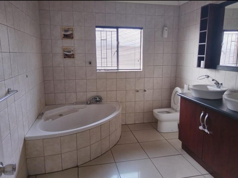 A functional bathroom featuring a corner bathtub, dual vessel sinks on a vanity cabinet, and tiled finishes throughout.