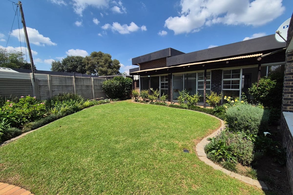 A well-maintained rear garden featuring a manicured lawn with brick edging, established landscaping, and a covered patio area with sliding glass doors.
