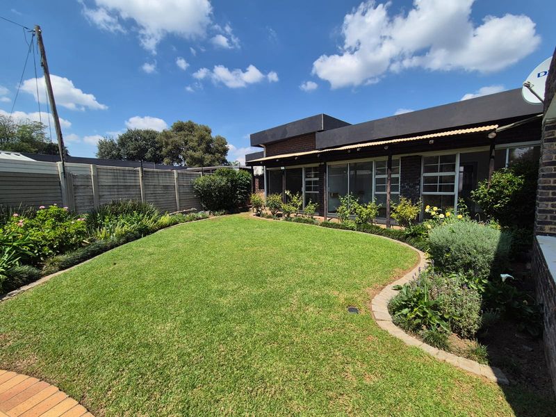 A well-maintained rear garden featuring a manicured lawn with brick edging, established landscaping, and a covered patio area with sliding glass doors.