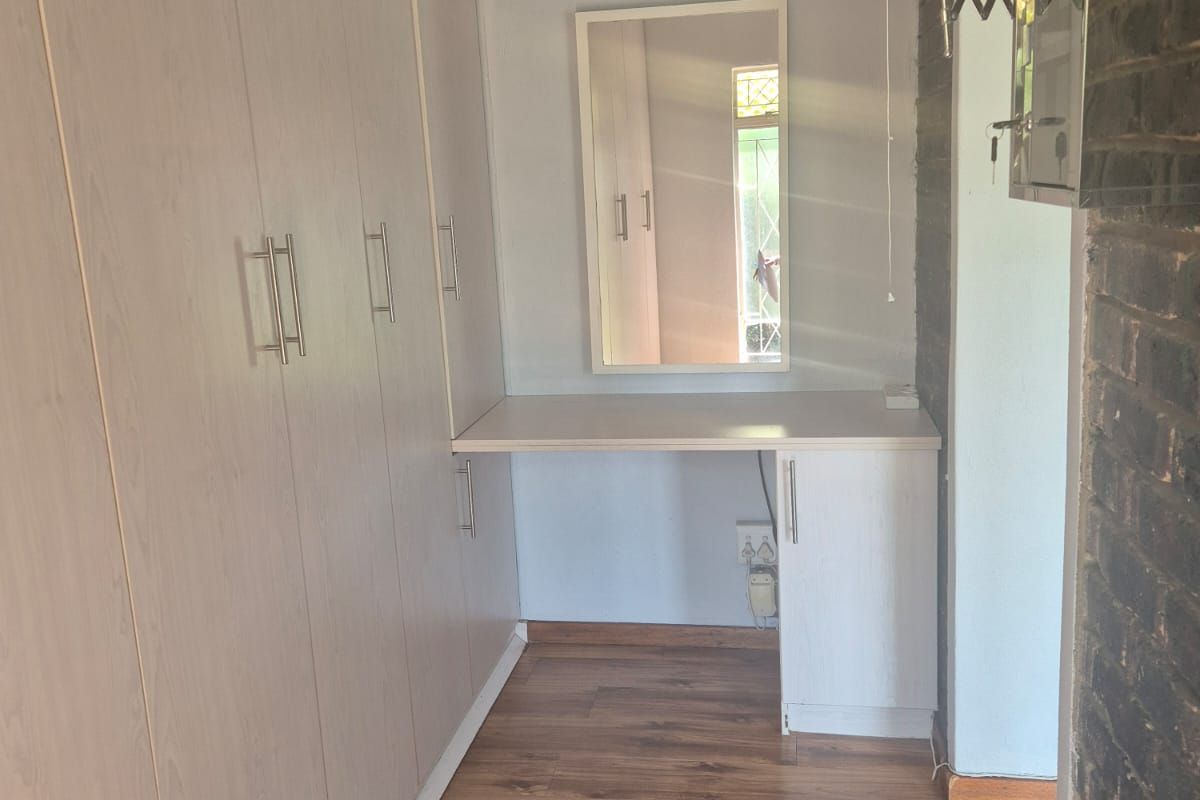 A bedroom dressing area featuring built-in cupboards, a vanity unit, and laminate flooring, accented by an exposed brick wall.