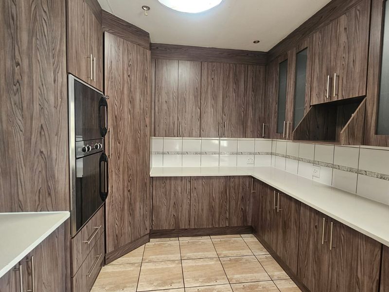 A functional kitchen featuring dark wood-grain cabinetry, stone countertops, a built-in oven, and neutral tiled flooring with a clean backsplash.