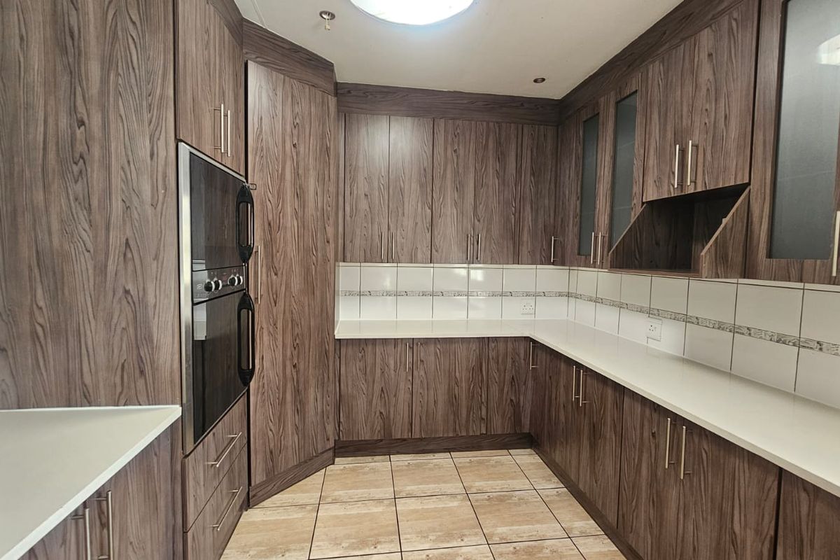 A functional kitchen featuring dark wood-grain cabinetry, stone countertops, a built-in oven, and neutral tiled flooring with a clean backsplash.
