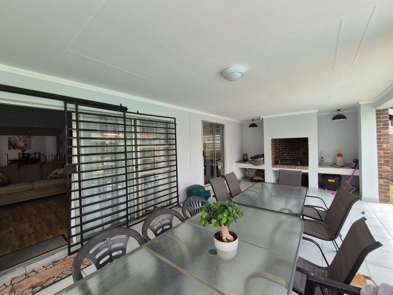 Covered patio area featuring a built-in braai, tiled flooring, and sliding security gate access to the main living space.