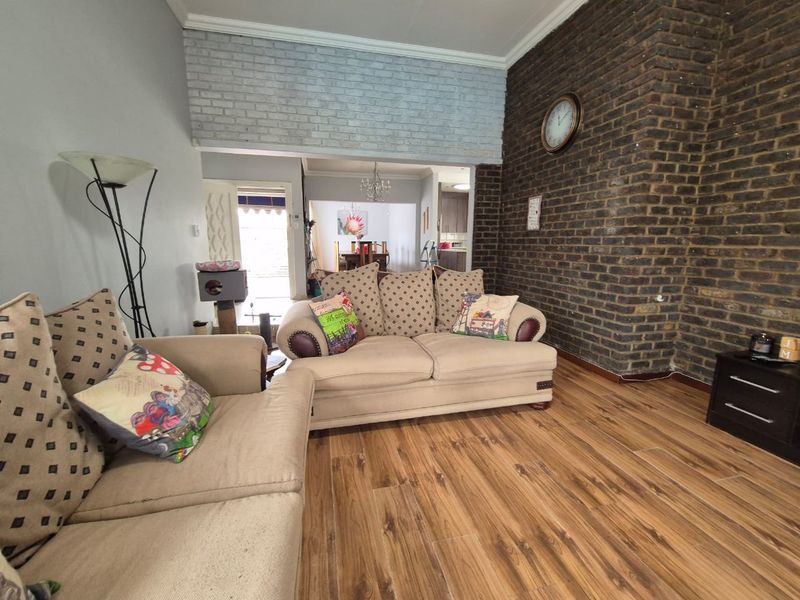 A living room featuring a prominent exposed brick wall, laminate flooring, and an open-plan layout leading to the dining area.