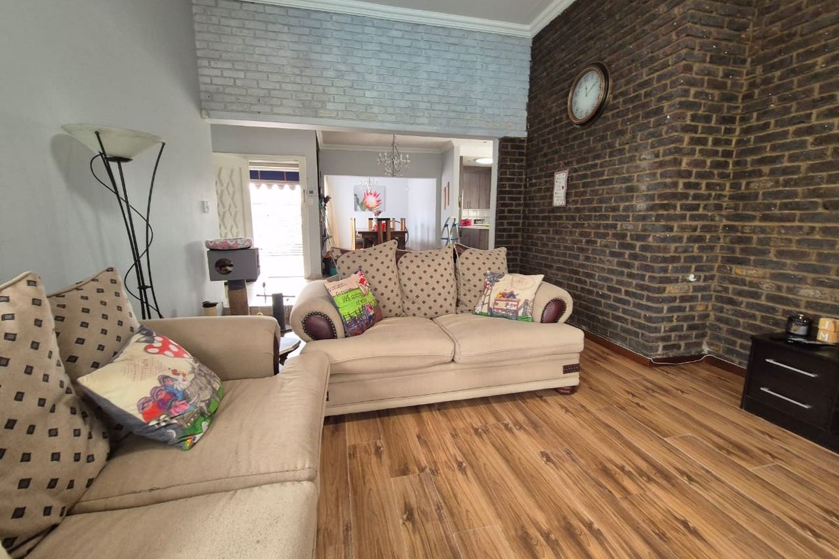 A living room featuring a prominent exposed brick wall, laminate flooring, and an open-plan layout leading to the dining area.