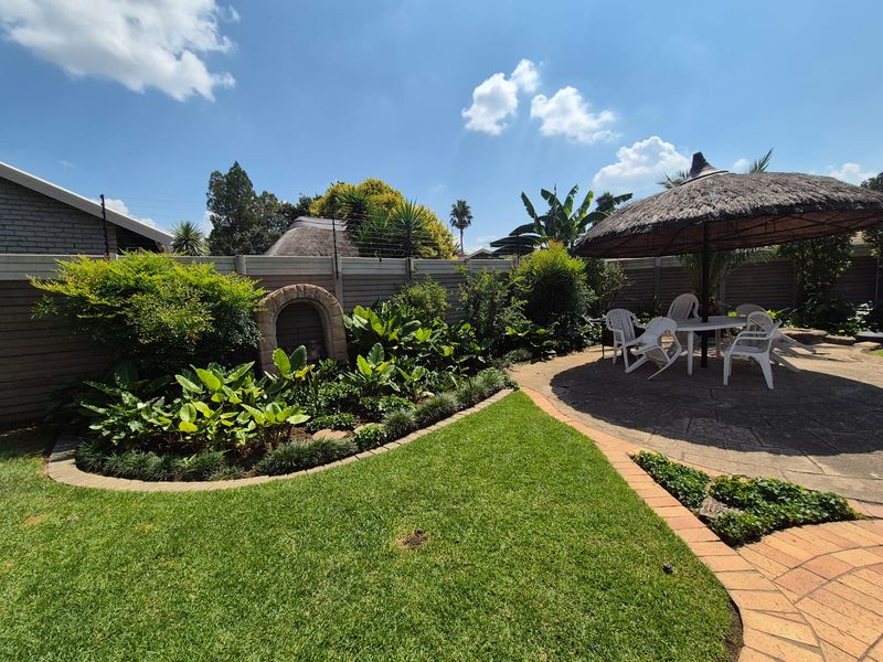 A well-maintained garden featuring a paved patio area, established landscaping, stone garden feature, and secure perimeter walling with electric fencing.