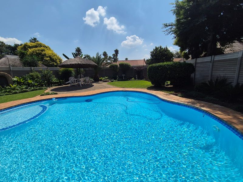 A well-maintained outdoor pool area featuring a clear swimming pool, paved surround, and established garden with boundary walling.