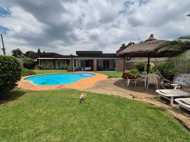 Spacious backyard featuring a swimming pool, covered patio area, and a traditional thatched lapa with a built-in pizza oven.