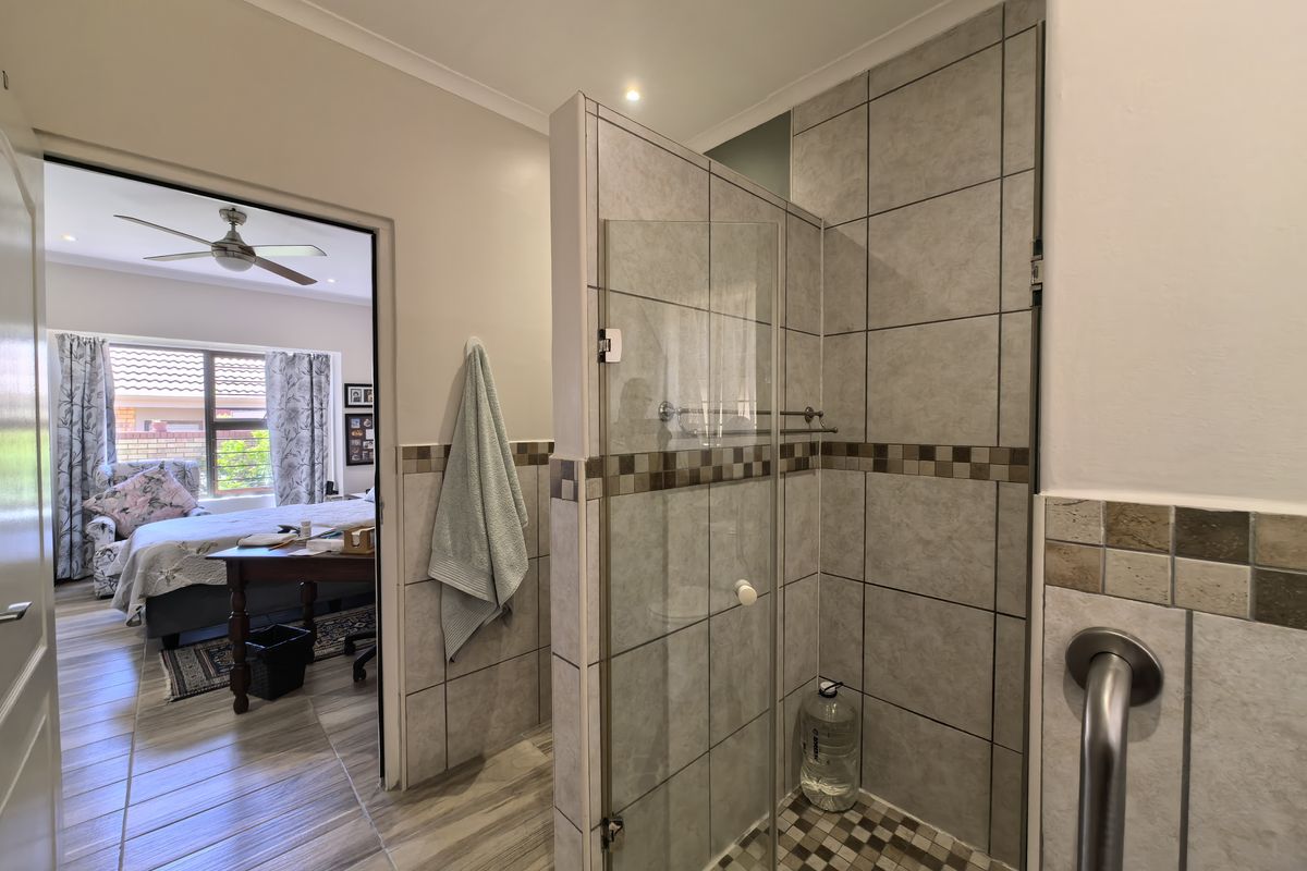 A functional bathroom featuring a walk-in shower with glass screen, mosaic floor tiling, and a convenient grab rail, with direct access to the bedroom.