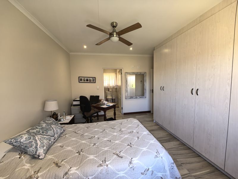 A well-maintained bedroom featuring extensive built-in cupboards, laminate flooring, a ceiling fan, and an en-suite bathroom access.