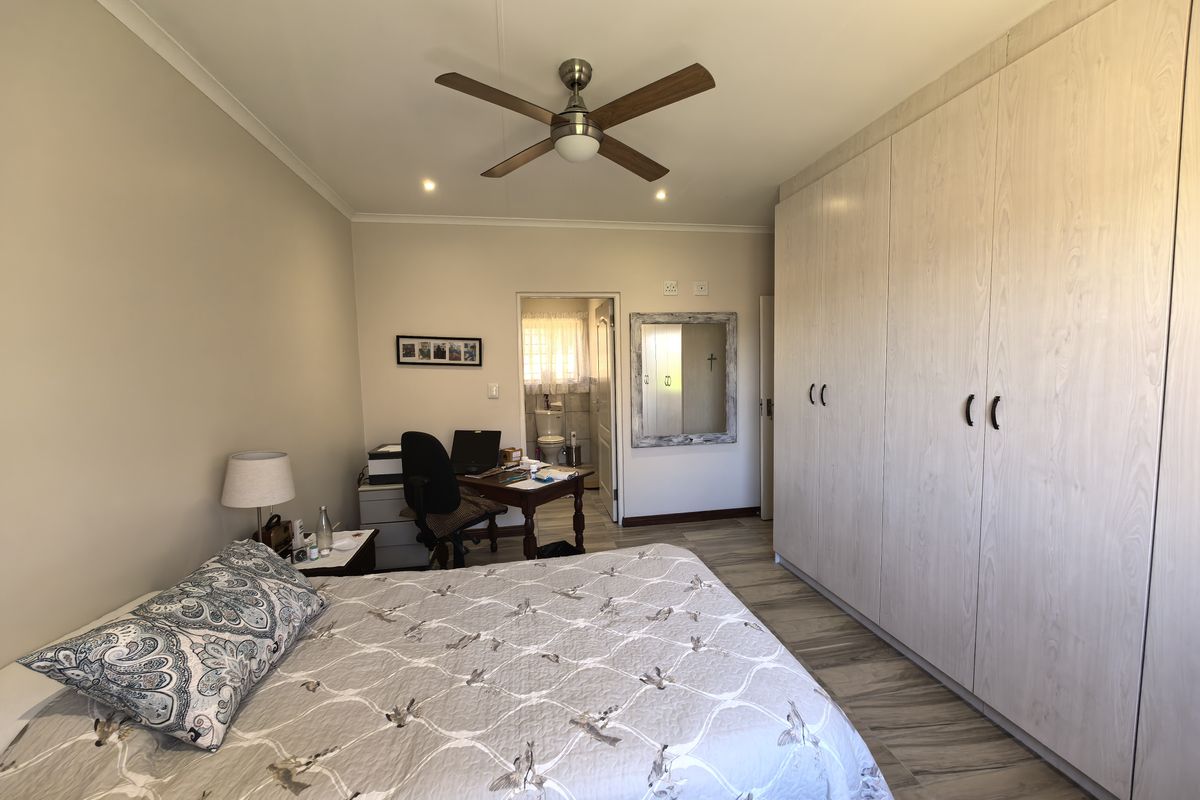 A well-maintained bedroom featuring extensive built-in cupboards, laminate flooring, a ceiling fan, and an en-suite bathroom access.