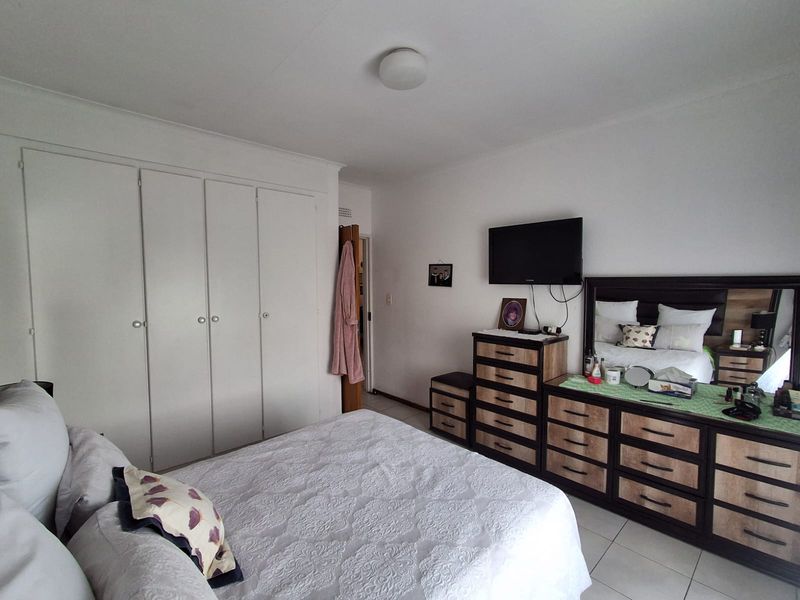A functional bedroom featuring built-in cupboards, tiled flooring, and a ceiling light fixture, offering a clean and practical living space.
