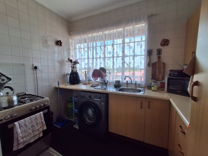 A functional kitchen featuring laminate cabinetry, a gas stove, and a stainless steel sink with a tiled backsplash and window security bars.