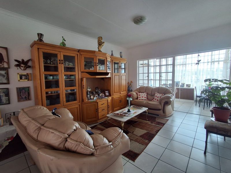 A spacious living room featuring tiled flooring and large windows that provide ample natural light, leading to an adjacent sunroom or patio area.