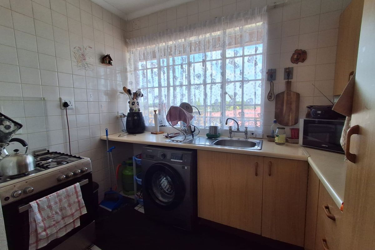 Functional kitchen featuring built-in cabinetry, laminate countertops, a stainless steel sink, and a gas stove, with tiled walls and security bars on the window.