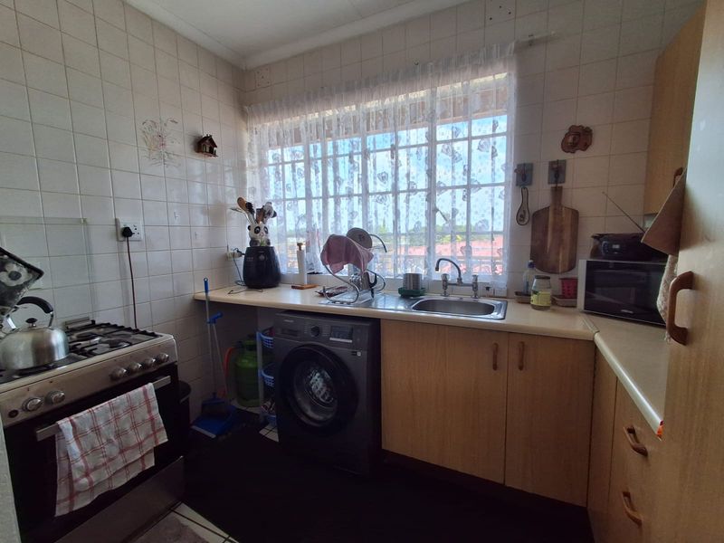 Functional kitchen featuring built-in cabinetry, laminate countertops, a stainless steel sink, and a gas stove, with tiled walls and security bars on the window.