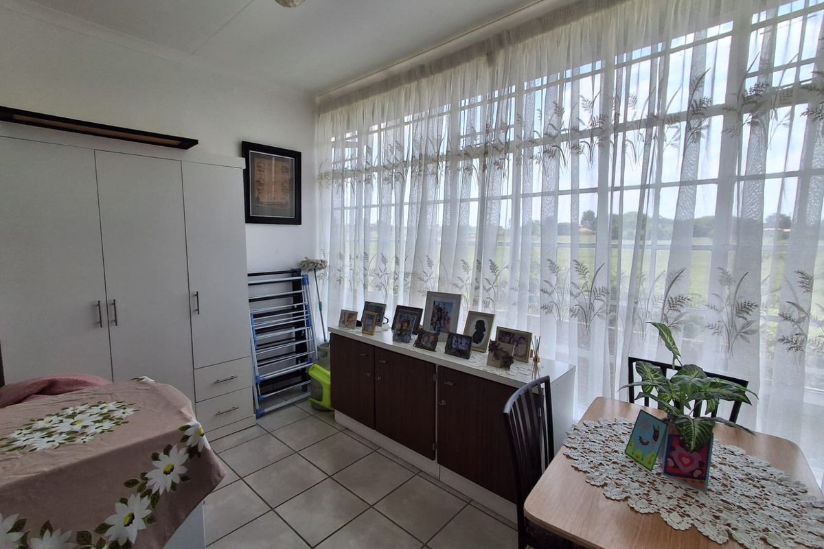 A bedroom featuring tiled flooring, a built-in wardrobe, and a large window with sheer curtains providing natural light.
