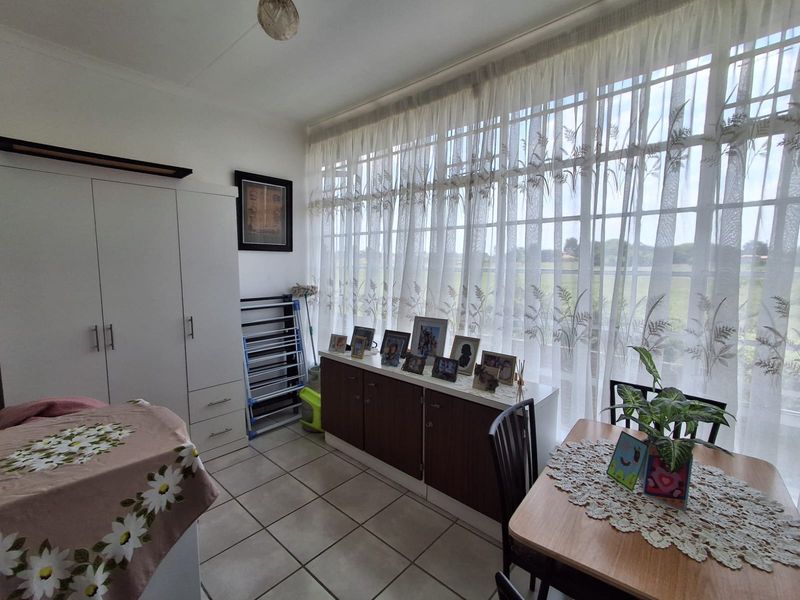 A bedroom featuring tiled flooring, a built-in wardrobe, and a large window with sheer curtains providing natural light.