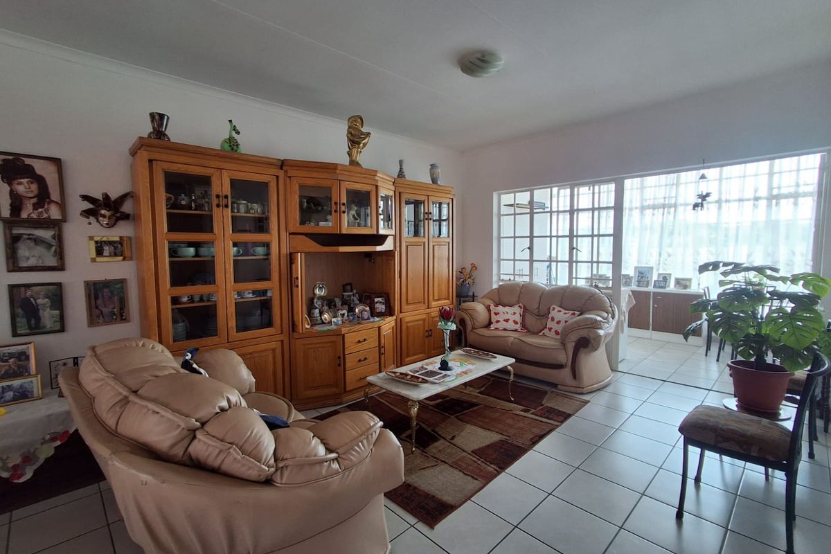 A spacious living room featuring tiled flooring, a large multi-pane window providing natural light, and coved ceiling details.