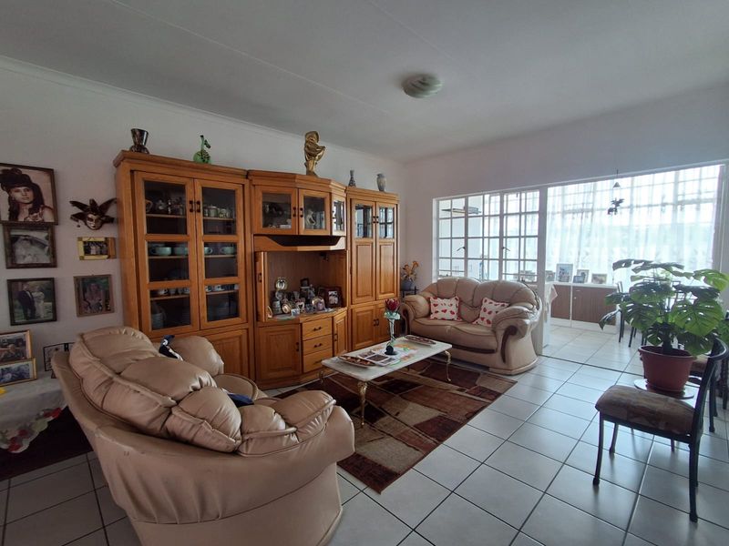 A spacious living room featuring tiled flooring, a large multi-pane window providing natural light, and coved ceiling details.