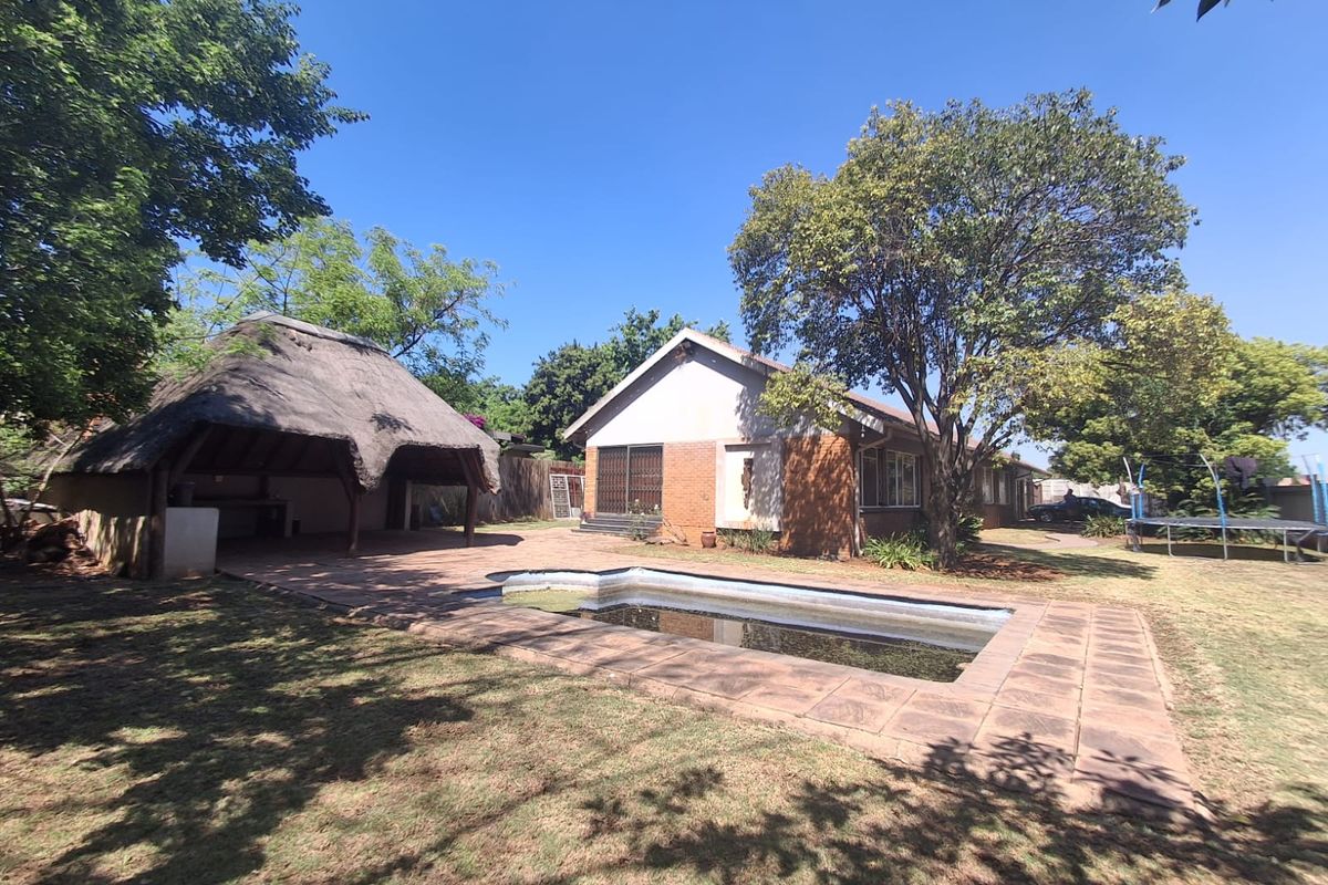 Rear exterior view featuring a swimming pool, paved patio area, and a traditional thatched lapa set within a spacious garden.
