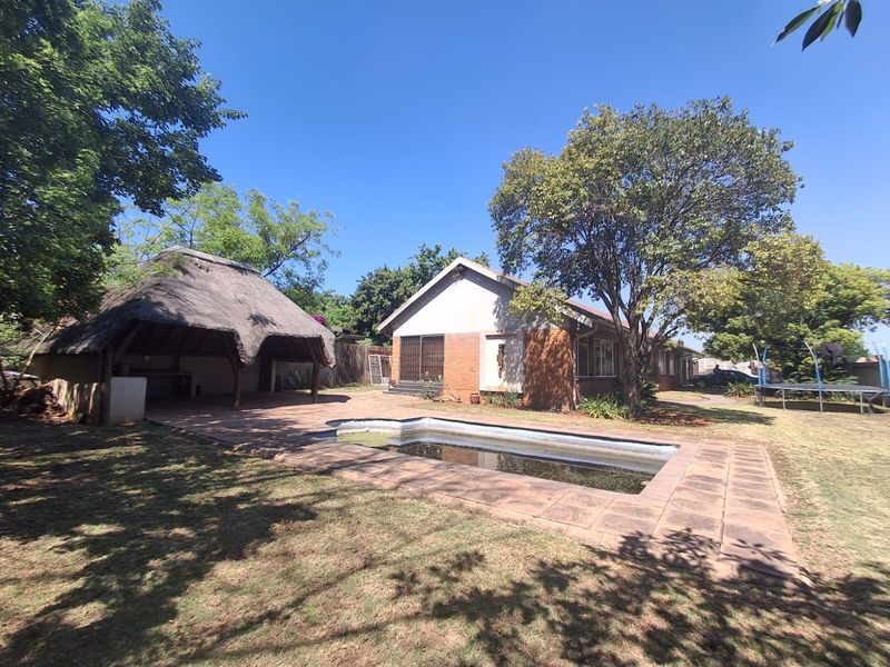 Rear exterior view featuring a swimming pool, paved patio area, and a traditional thatched lapa set within a spacious garden.