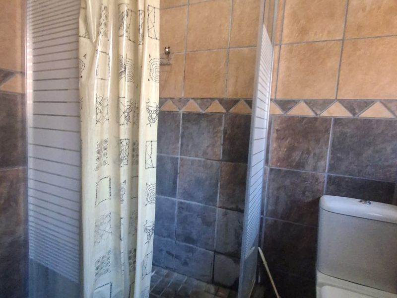 A functional bathroom featuring a corner shower enclosure with tiled surround and a standard toilet.