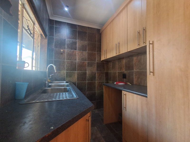 A functional scullery featuring built-in wooden cabinetry, dark laminate countertops, a double bowl stainless steel sink, and tiled wall finishes.