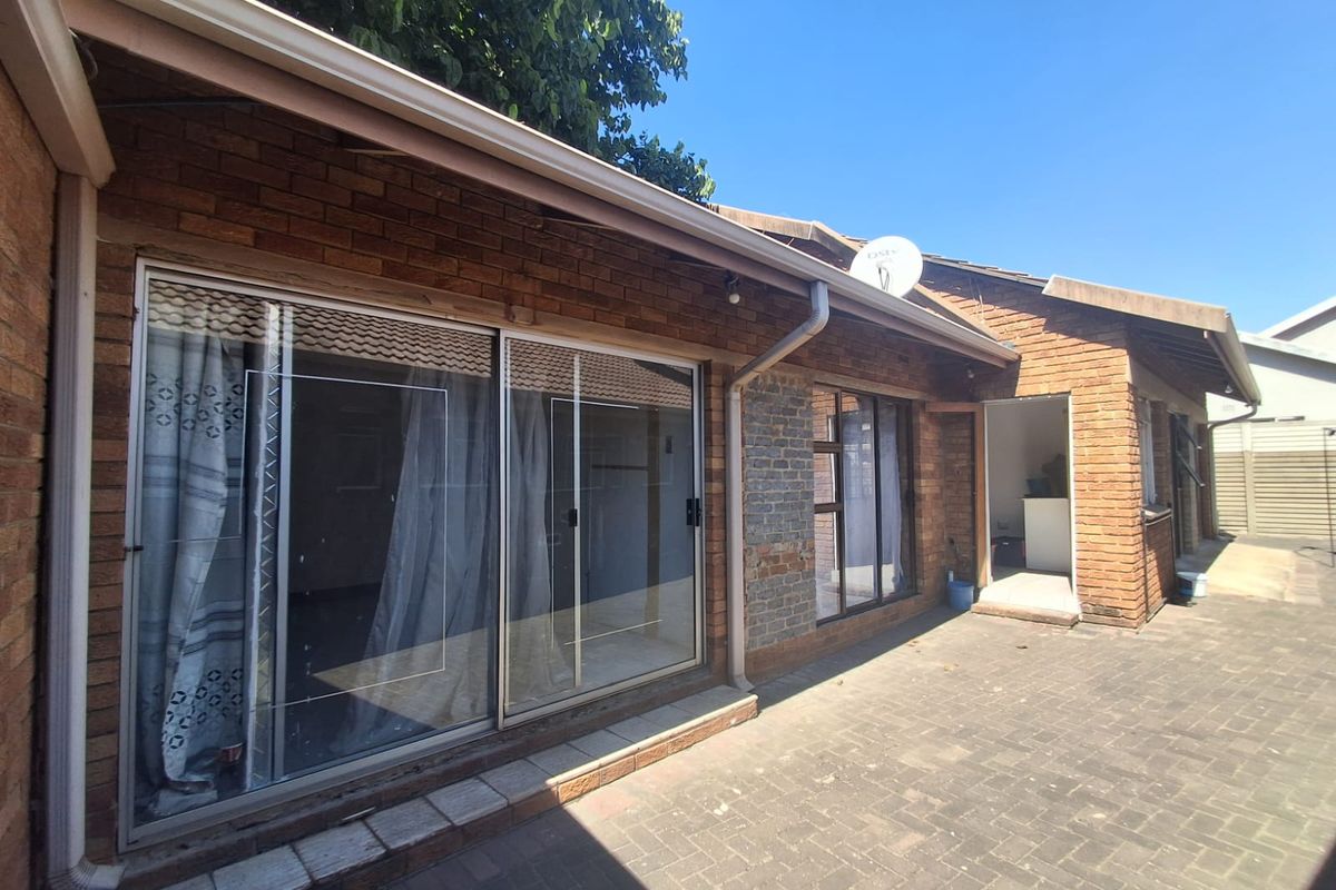 Rear exterior view of the house featuring brick facade, paved patio area, and sliding glass door access.