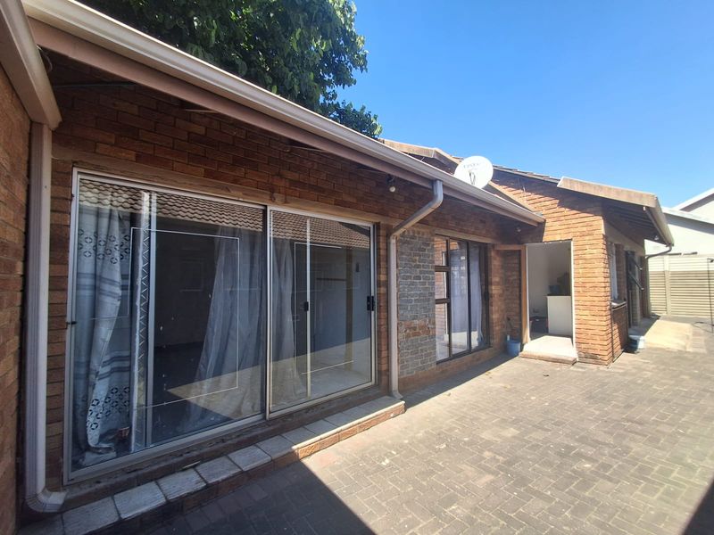 Rear exterior view of the house featuring brick facade, paved patio area, and sliding glass door access.
