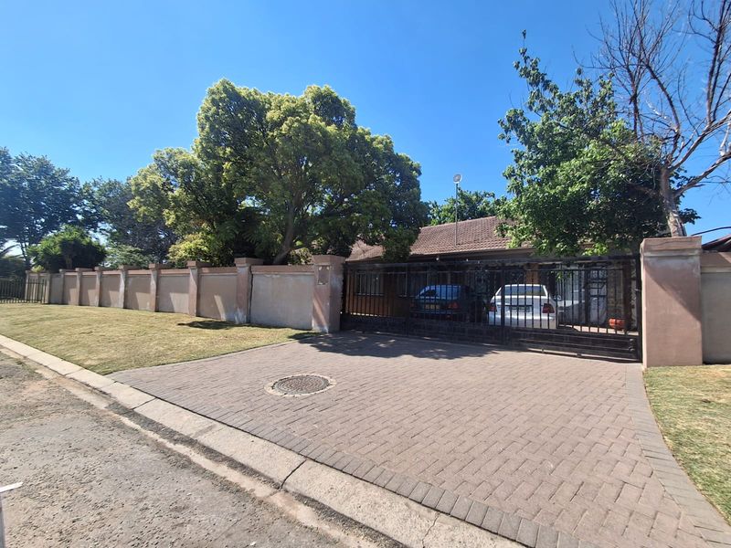 Front exterior view of the property featuring a paved driveway, secure metal gate, and a perimeter wall with a tiled roof house behind.