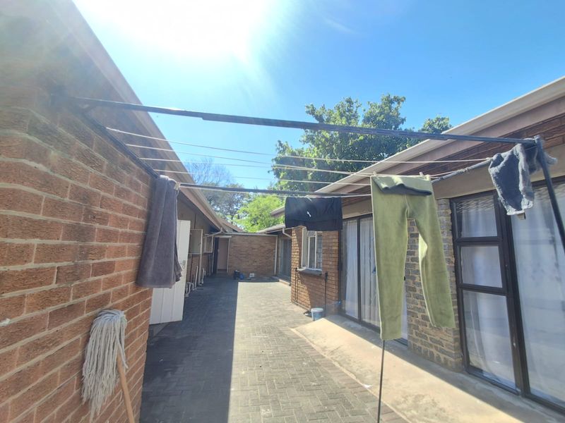 A paved rear courtyard area featuring brick exterior walls, sliding glass door access, and a functional outdoor washing line.