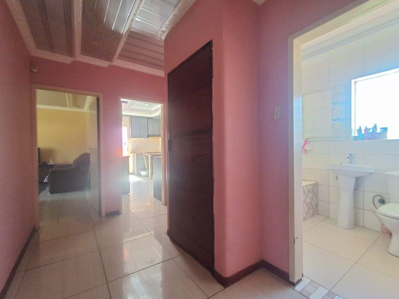 A central hallway connecting multiple rooms, featuring tiled flooring and access to a bathroom with a pedestal basin and toilet.