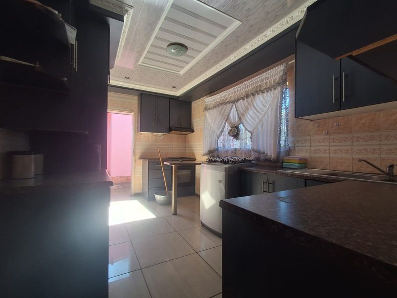 A functional kitchen featuring dark built-in cabinetry, tiled backsplash, and tiled flooring, offering a practical layout with direct access to an exterior area.