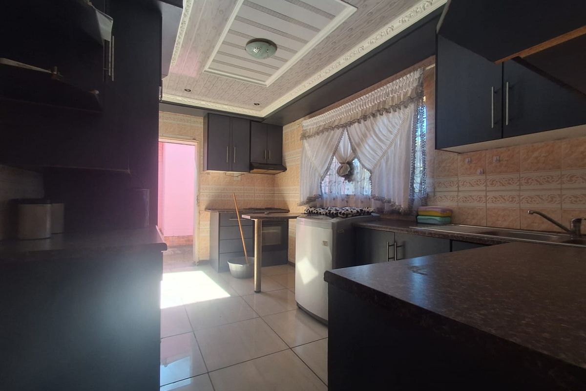 A functional kitchen featuring dark built-in cabinetry, tiled backsplash, and tiled flooring, offering a practical layout with direct access to an exterior area.