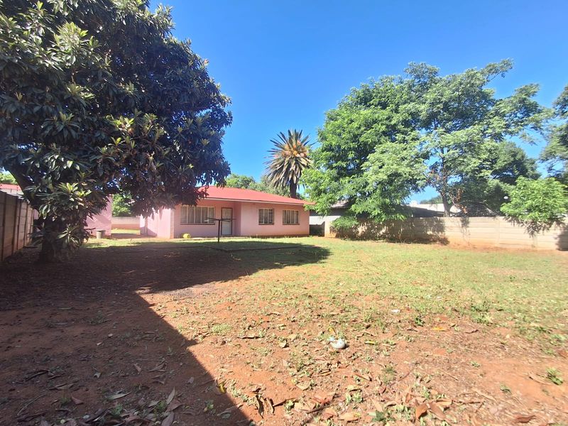 A view of the rear garden and the back elevation of the house, featuring a large lawn area and perimeter boundary walls.
