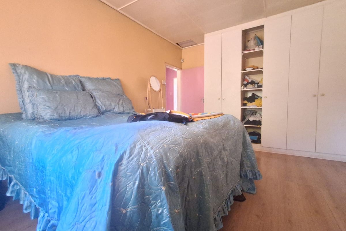 A bedroom featuring laminate flooring and a built-in wardrobe with open shelving, requiring cosmetic updates to the walls and ceiling.