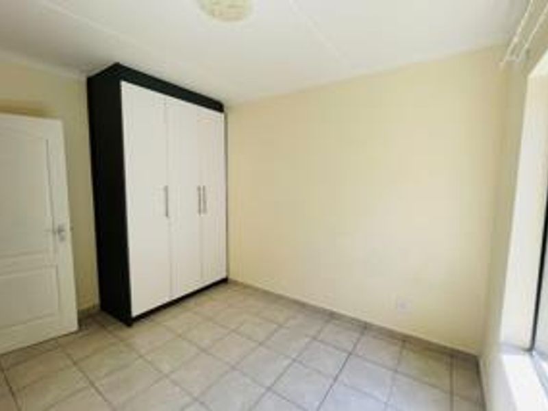 A clean, empty bedroom featuring neutral wall tones, tiled flooring, and a modern built-in wardrobe with contrasting black and white finishes.