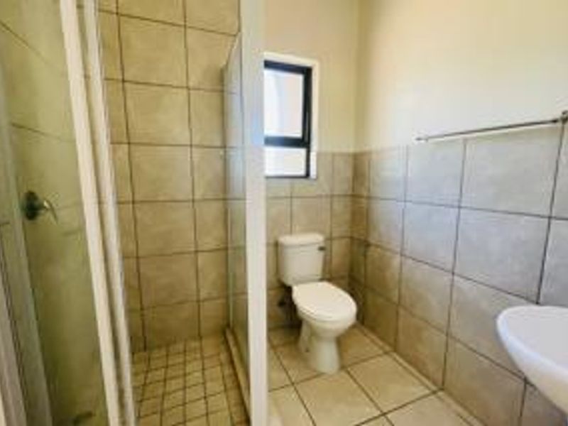 A functional bathroom featuring a shower enclosure, toilet, and basin with neutral wall and floor tiling.