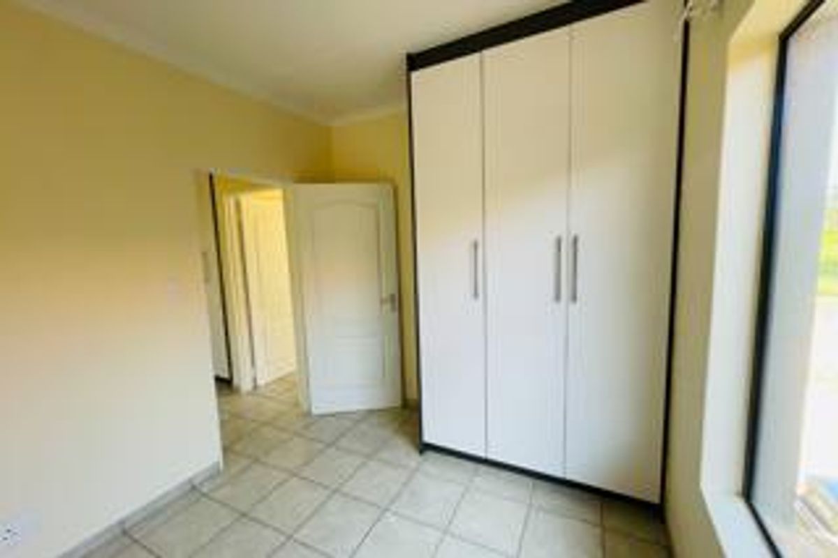 A bright, empty bedroom featuring neutral walls, tiled flooring, and modern white built-in cupboards with clean lines.