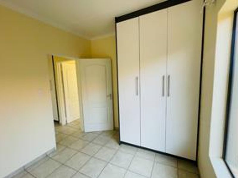 A bright, empty bedroom featuring neutral walls, tiled flooring, and modern white built-in cupboards with clean lines.