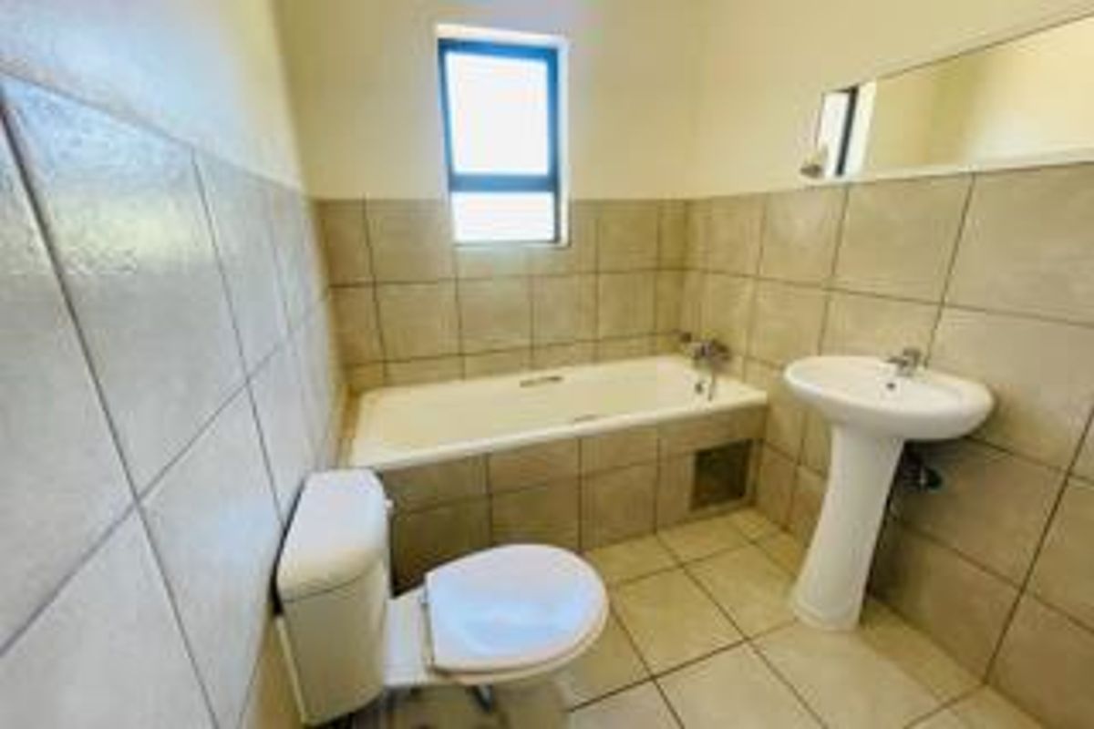 A functional bathroom featuring a bathtub with tiled surround, a pedestal basin, and a toilet, finished with neutral wall and floor tiles.