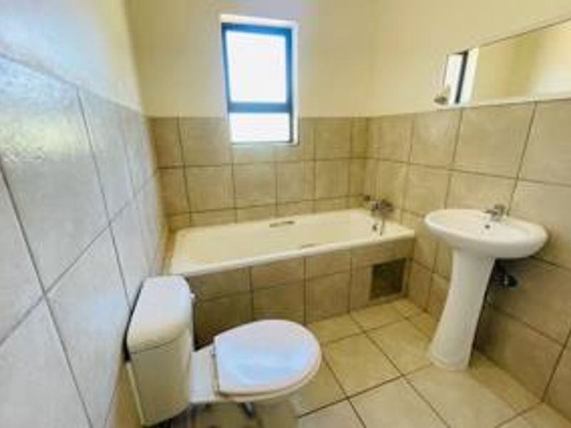 A functional bathroom featuring a bathtub with tiled surround, a pedestal basin, and a toilet, finished with neutral wall and floor tiles.