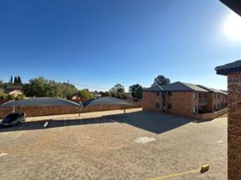 Exterior view of the apartment complex featuring a paved parking area with shade cloth carports and brick building facades.