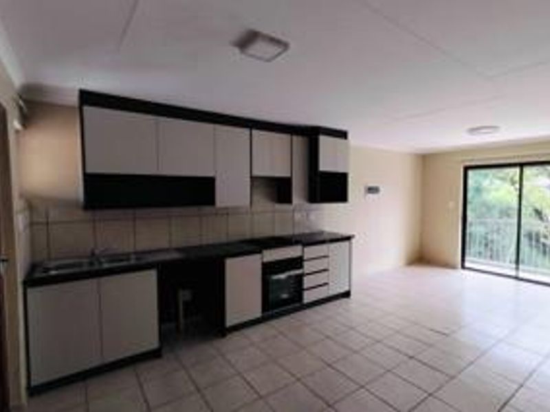 Open-plan kitchen and living area featuring modern two-tone cabinetry, built-in oven, tiled flooring, and direct access to a balcony through sliding glass doors.