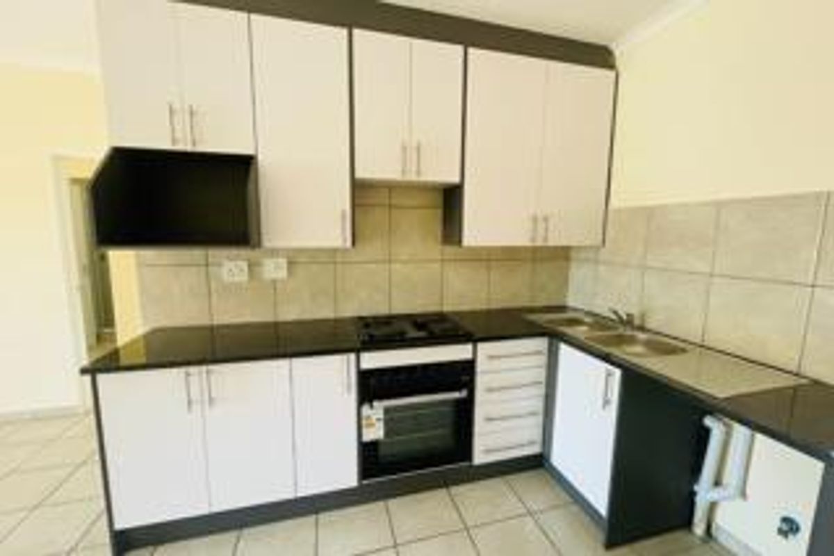 A functional kitchen featuring white cabinetry, dark countertops, a built-in oven and hob, and a double sink with tiled backsplash.