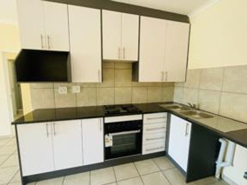 A functional kitchen featuring white cabinetry, dark countertops, a built-in oven and hob, and a double sink with tiled backsplash.